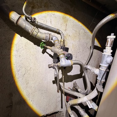 Hausanschluss mit Absperrventilen und Wasserzähler im Keller, ausgeleuchtet von einer Arbeitsleuchte