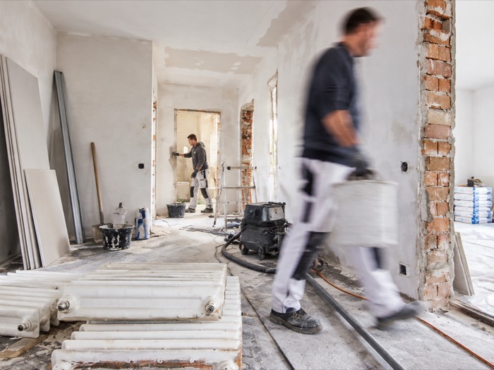 Wohnung im Rohbauzustand während einer Sanierung: freigelegtes Mauerwerk, ausgebaute Heizkörper und ein Handwerker beim Materialtransport